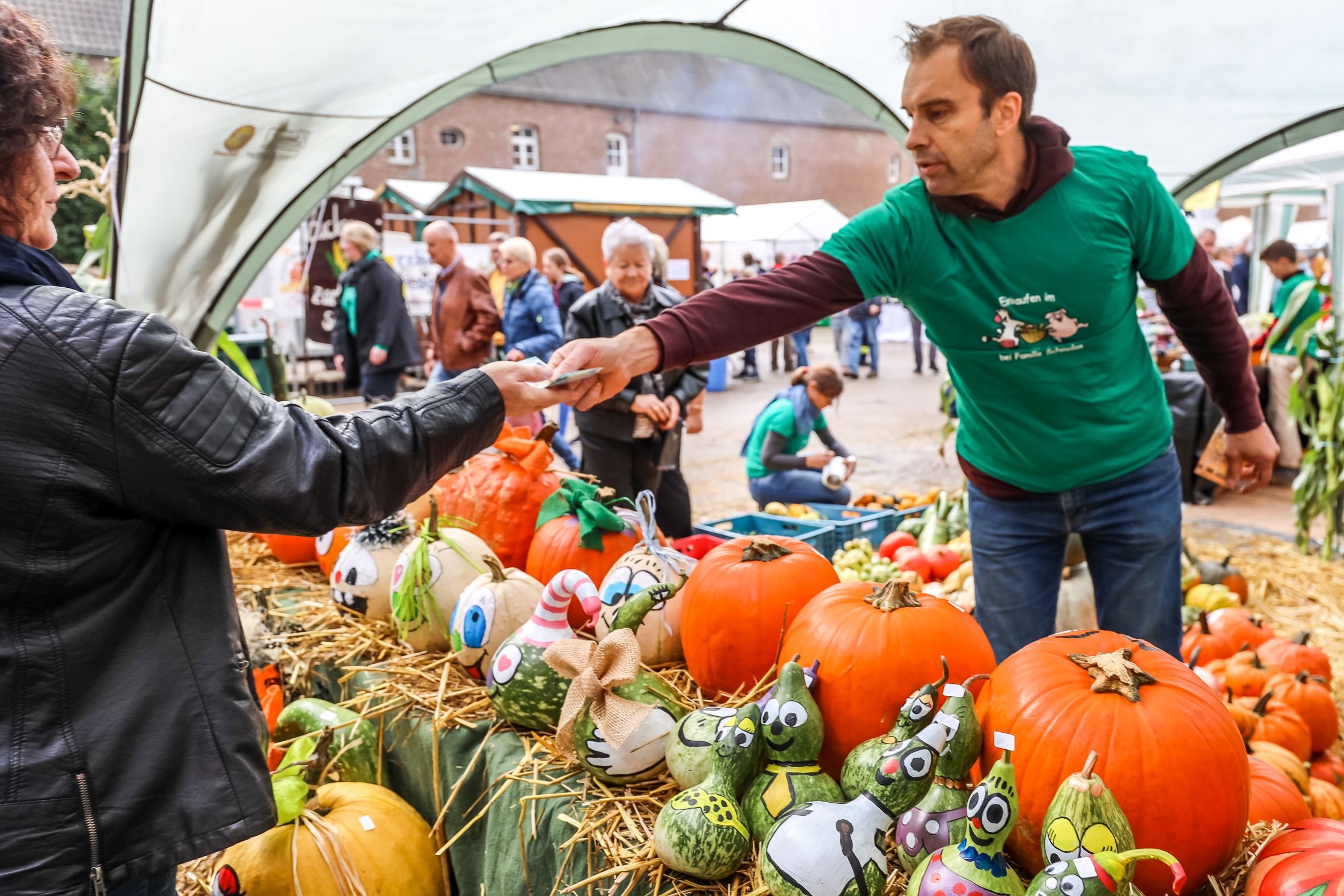 Stand mit Kürbissen auf dem Bauernmarkt auf Hohenbusch - eine Kundin nimmt Wechselgeld entgegen