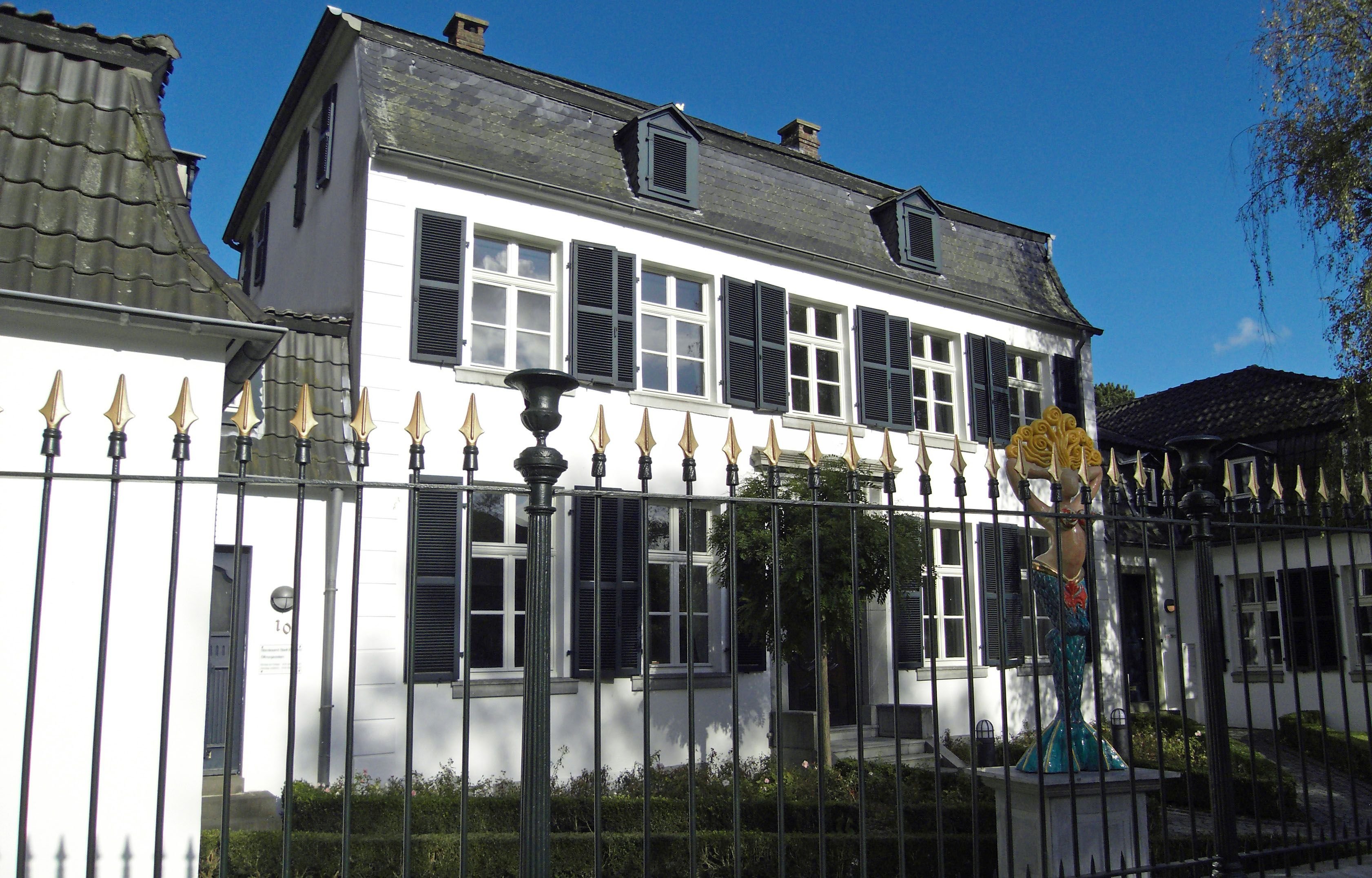 Außenansicht von Haus Spiess mit einer Kunst-Skulptur hinter dem Zaun