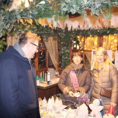 Ein Gast des Adventsdorfes steht an einem Verkaufsstand mit zwei Verkaufskräften