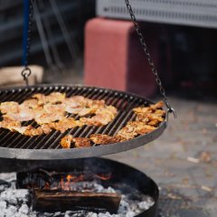 Auf einem Schwenkgrill wird Fleisch gegrillt.