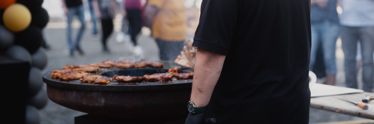 Jemand steht an einem Grill und grillt Fleisch