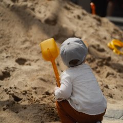 Ein Kind sitzt mit einer Schüppe in der Hand vor einem Sandhügel.