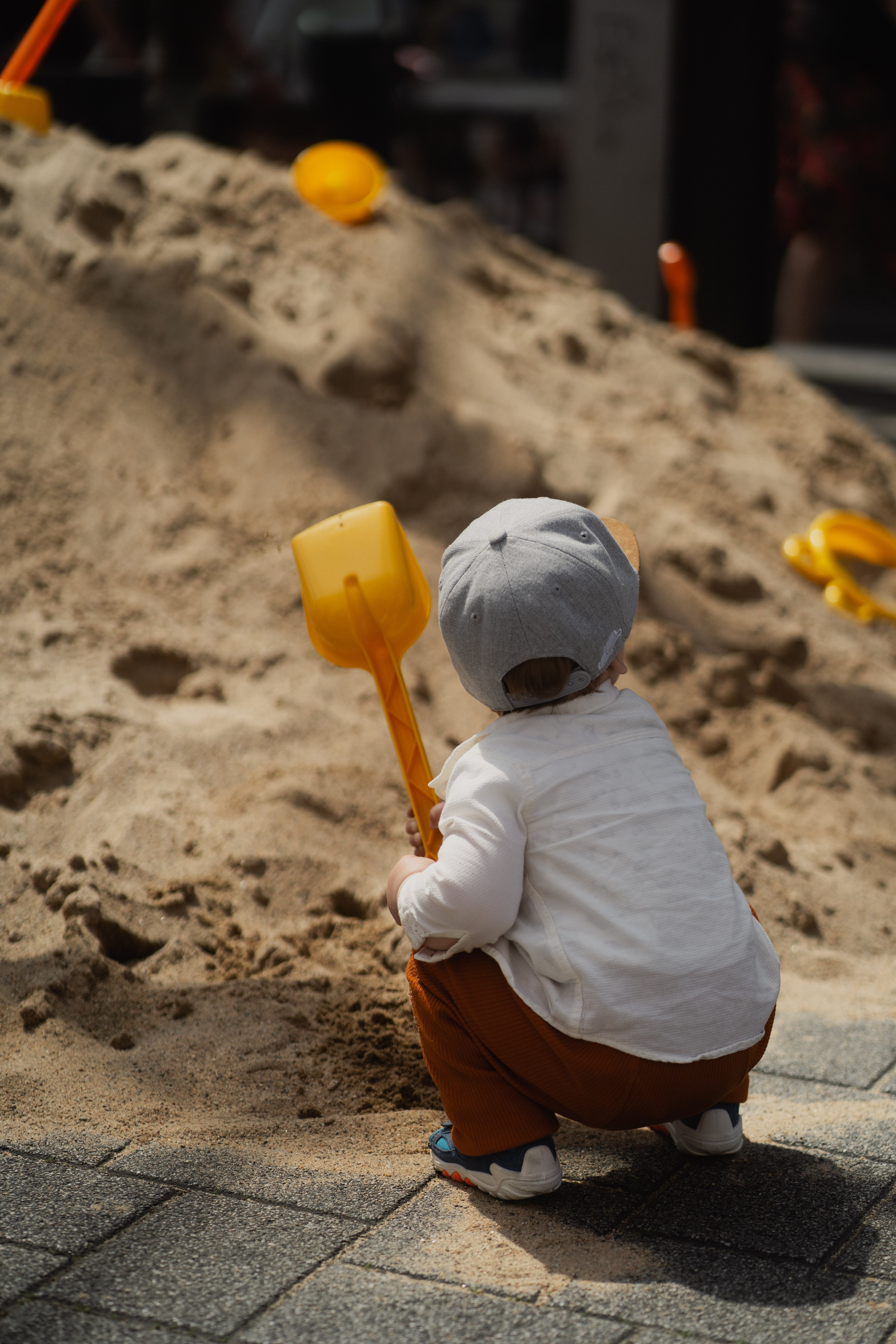Ein Kind sitzt mit einer Schüppe in der Hand vor einem Sandhügel.