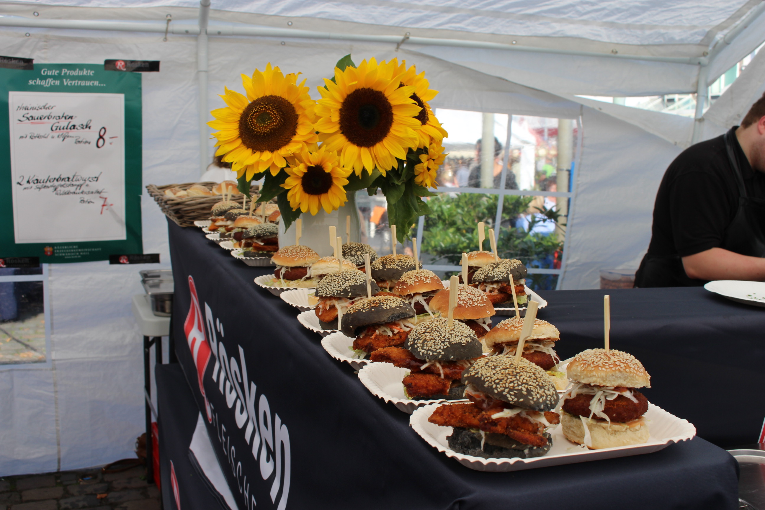 Auf einer Theke liegen viele Burger. Dazwischen steht ein Strauß mit Sonnenblumen.