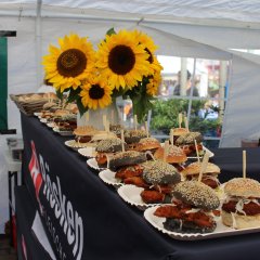 Auf einer Theke liegen viele Burger. Dazwischen steht ein Strauß mit Sonnenblumen.