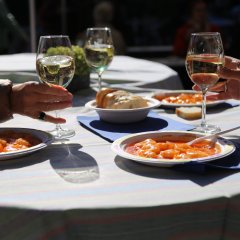 Auf einem Tisch stehen drei Teller mit Speisen und drei Gläser mit Wein. In der Mitte eine Schale mit Baguette.