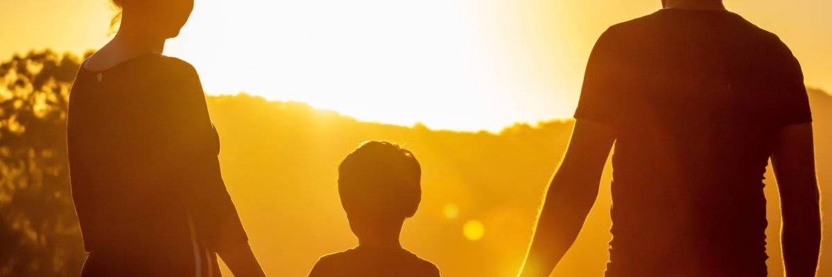 Mann, Frau und Kind stehen vor einem Sonnenuntergang