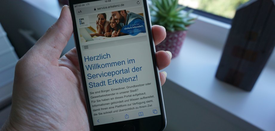 Jemand hält ein Smartphone in der Hand. Geöffnet ist die Seite Serviceportal der Stadt Erkelenz.