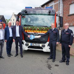 Gruppenbild vor Feuerwehrfahrzeug mit Schlüsselübergabe