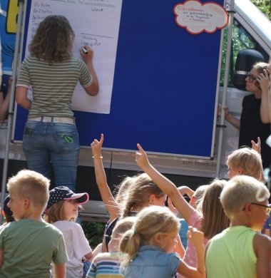 Kinder zeigen auf, im Hintergrund Pinnwand mit Zettel