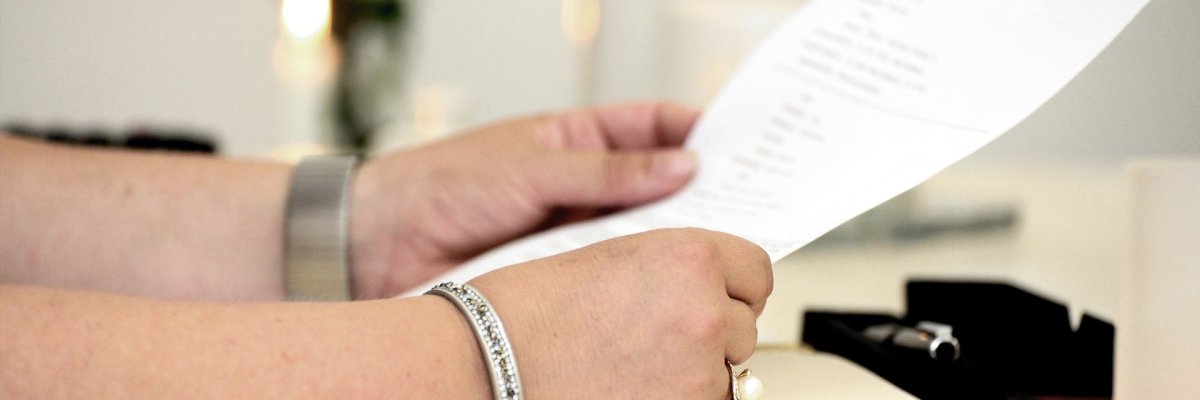 Person sitzt an einem Tisch und hält einen Zettel in der Hand