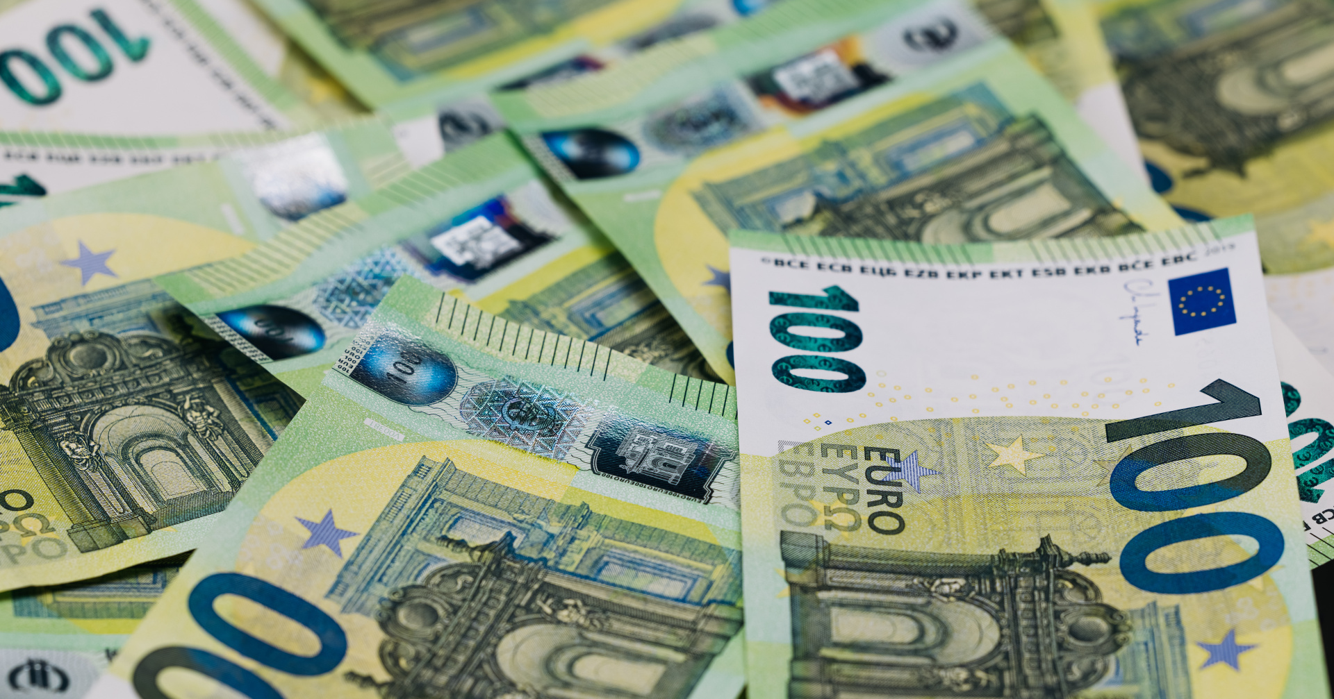 Close-up view of scattered 100 euro banknotes on a flat surface, showcasing intricate designs and security features of European currency