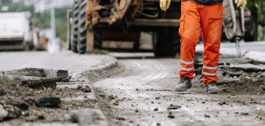 Construction worker repairs the street in urban area during daylight hours with heavy machinery nearby