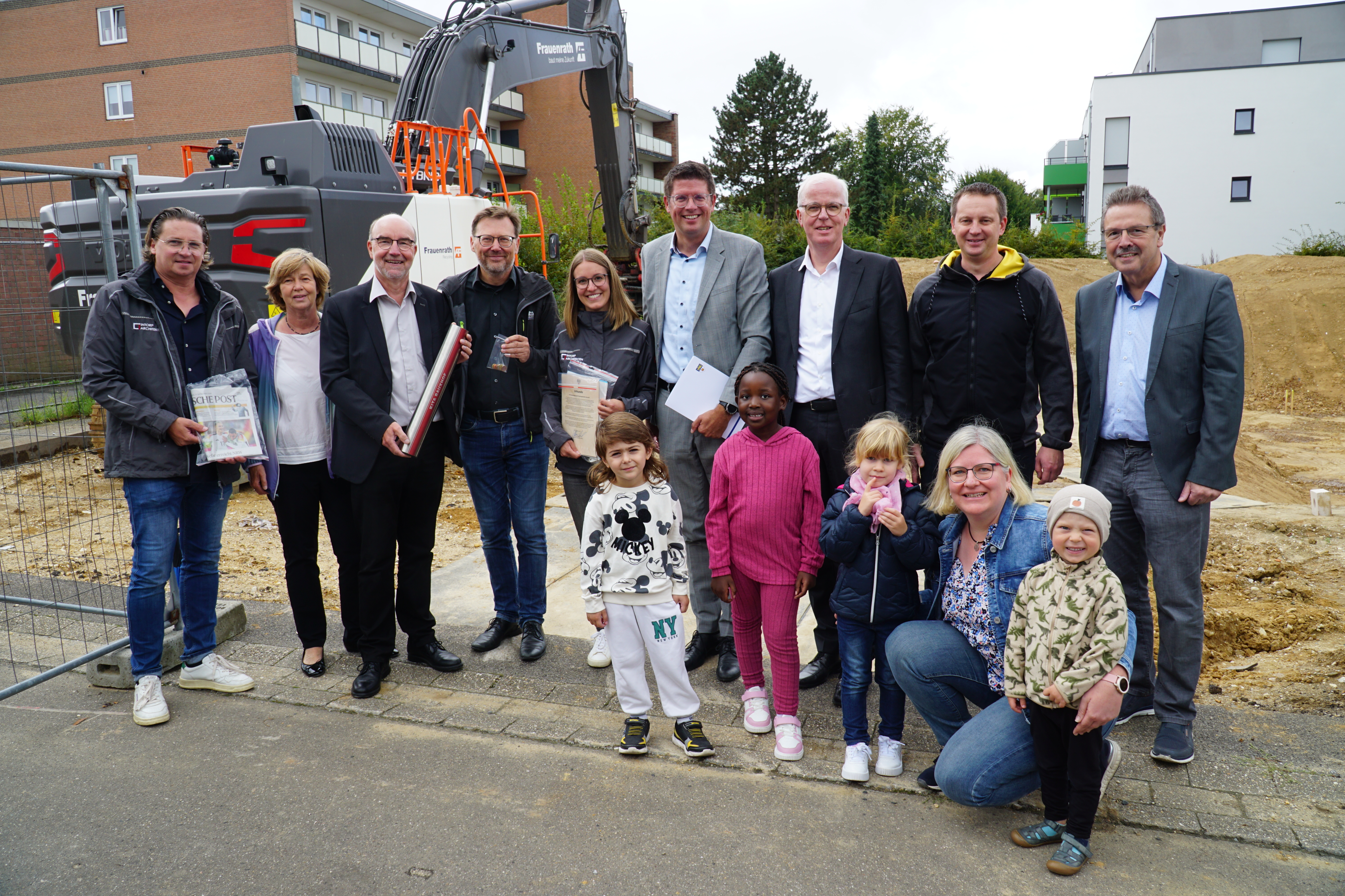 Beteiligte aus Rathaus und Politik sowie dem Architekturbüro füllten gemeinsam mit Kita-Kindern eine Zeitkapsel, die Bürgermeister Stephan Muckel zusammen mit dem Grundstein in der Erde vergrub.