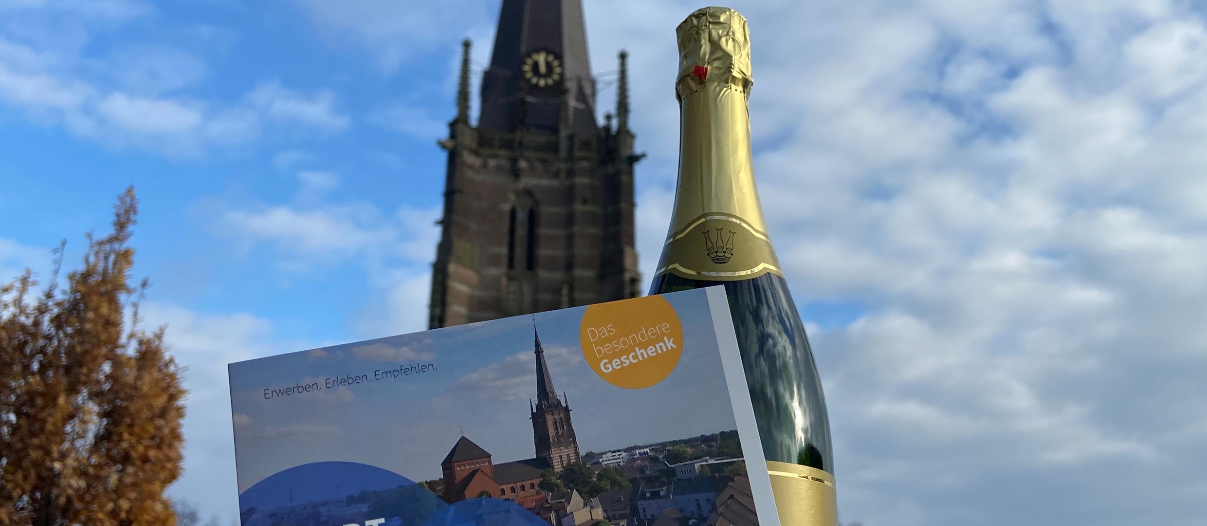 Stadtgutschein und Sekt, im Hintergrund der Kirchturm Sankt Lambertus