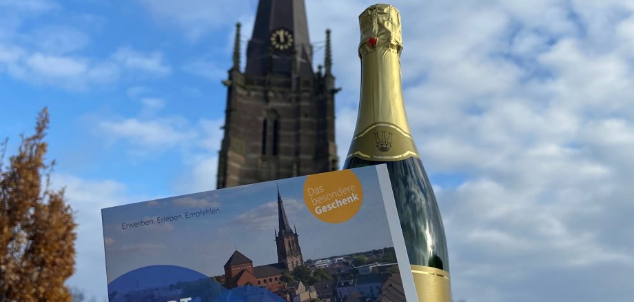 Stadtgutschein und Sekt, im Hintergrund der Kirchturm Sankt Lambertus