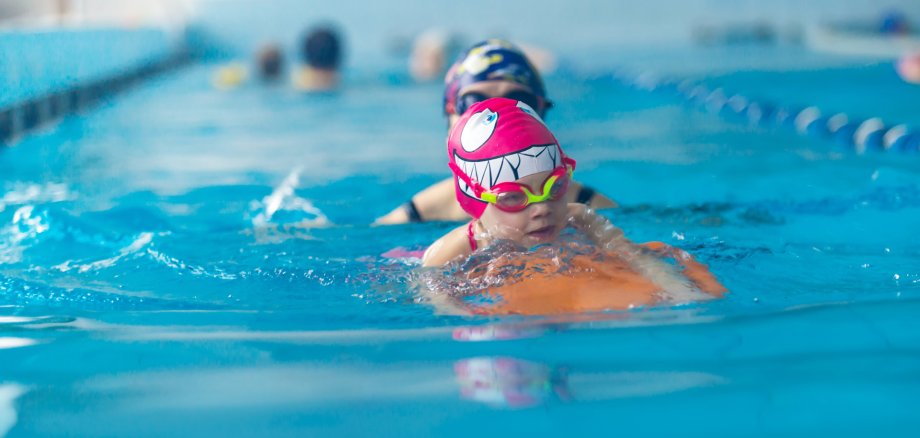 Portrait of mother or coach learning to swim with flutter board little girl at the public swimming-pool. Space for text