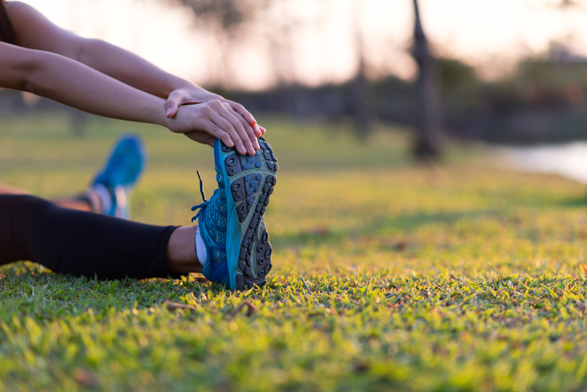 Woman stretching legs in green park at sunset after workout Woman stretching legs in green park at sunset after workout