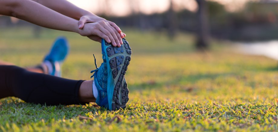 Woman stretching legs in green park at sunset after workout